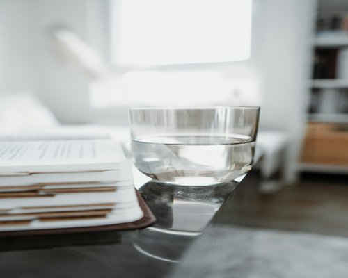 A stack of standard printed design books resting near a glass of fresh water on a clean surface